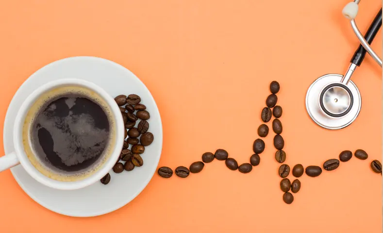 Taza de café y granos formando una línea de ritmo cardíaco junto a un estetoscopio para mostrar los beneficios del café de especialidad para tu salud.