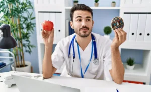 Médico decidiendo entre una manzana y una dona para explicar cómo controlar el colesterol y triglicéridos.