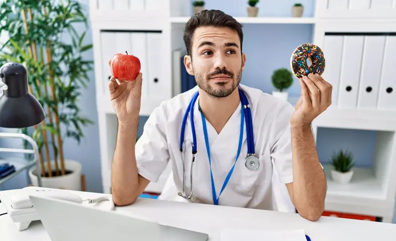 Médico decidiendo entre una manzana y una dona para explicar cómo controlar el colesterol y triglicéridos.